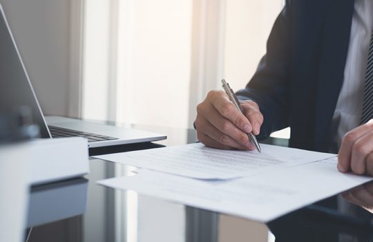 Signing contract, business agreement, deal concept. Businessman carefully reading terms and conditions before signing official business contract, formal document at modern office with laptop computer on table.